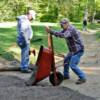 Doug Tipton dumps a load of gravel and dirt into the walkway while J.T. Tipton gets ready to drill a hole in a locust log for a peg that will hold it in place.